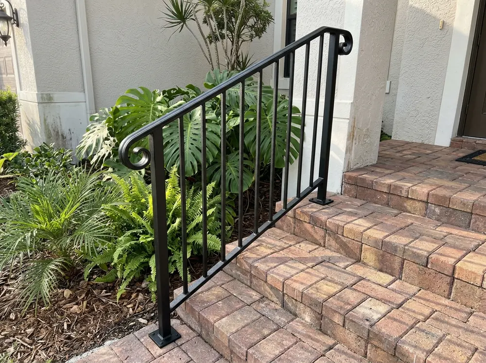 Black galvanized steel railing with simple scroll detail on brick-paver entry steps